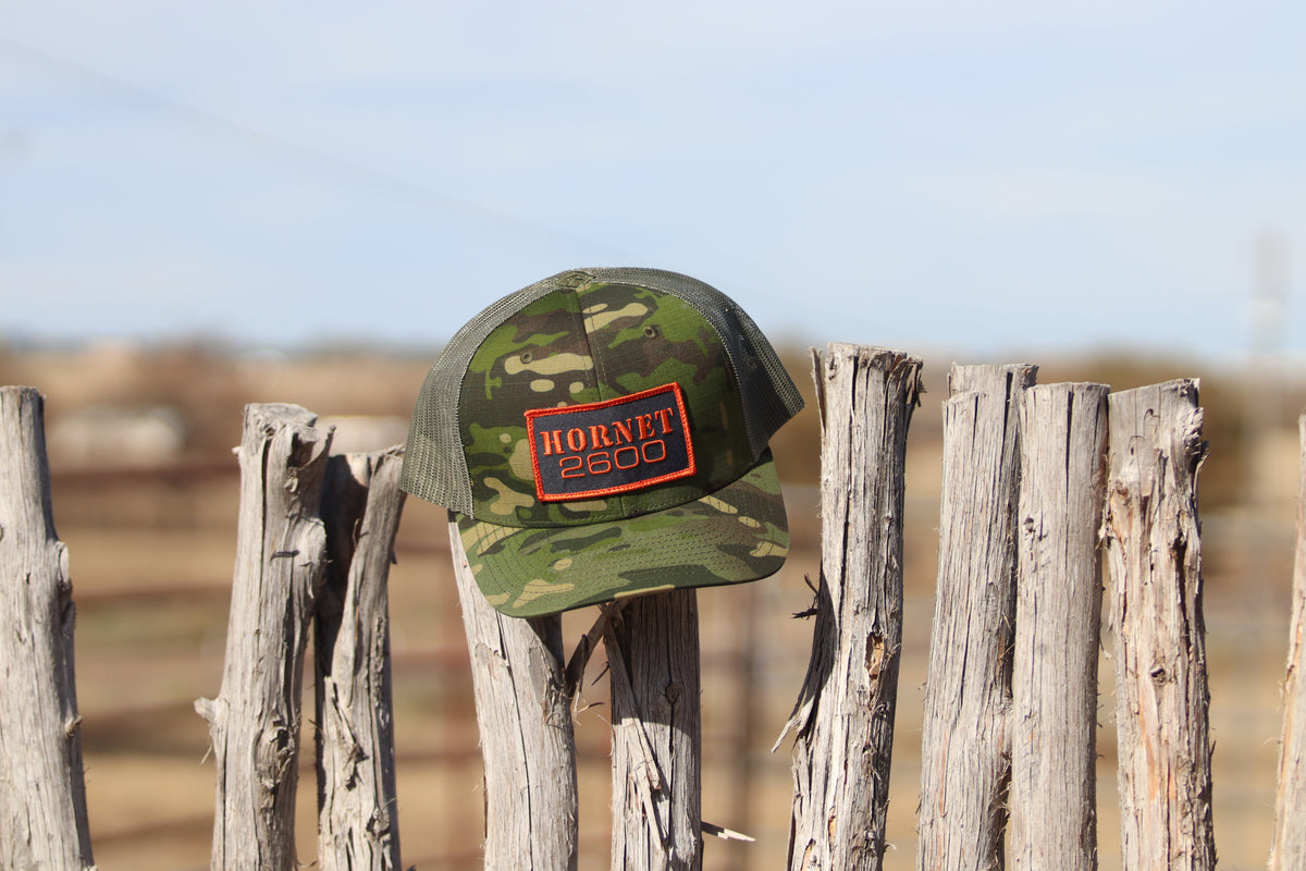 Camouflage cap with 'Hornet' logo on a wooden fence